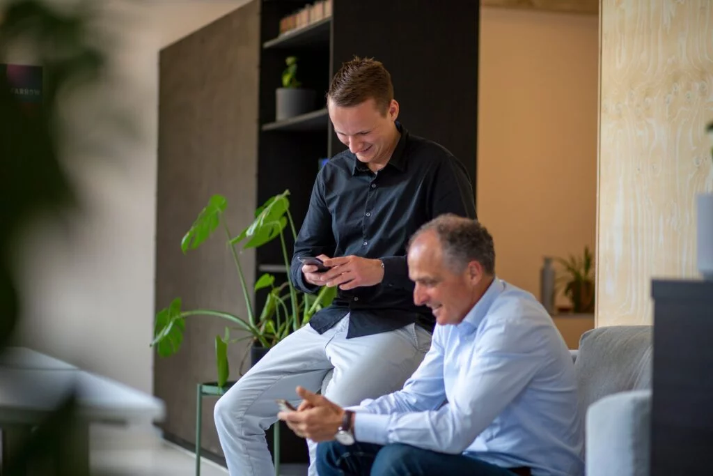Tom en Richard zittend op bank, kijkend naar telefoon